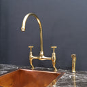 Unlacquered brass curved legs bridge faucet – installed over farmhouse sink